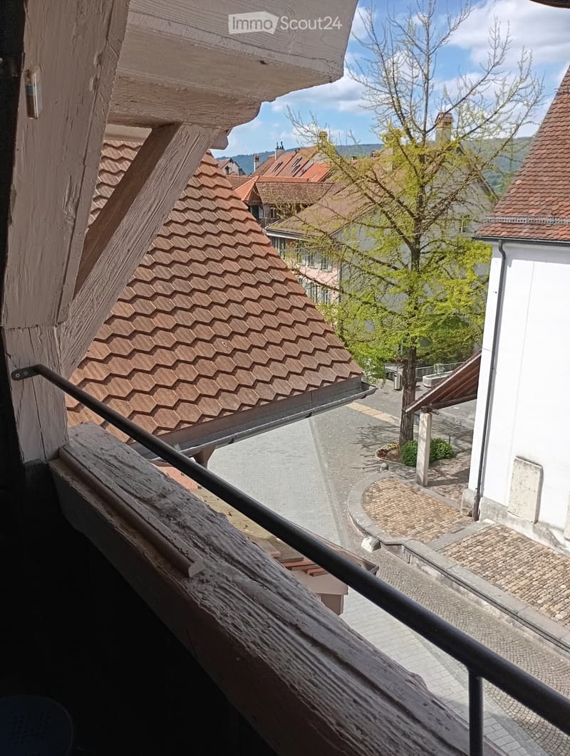 balcony with wooden railing, view of street and tree