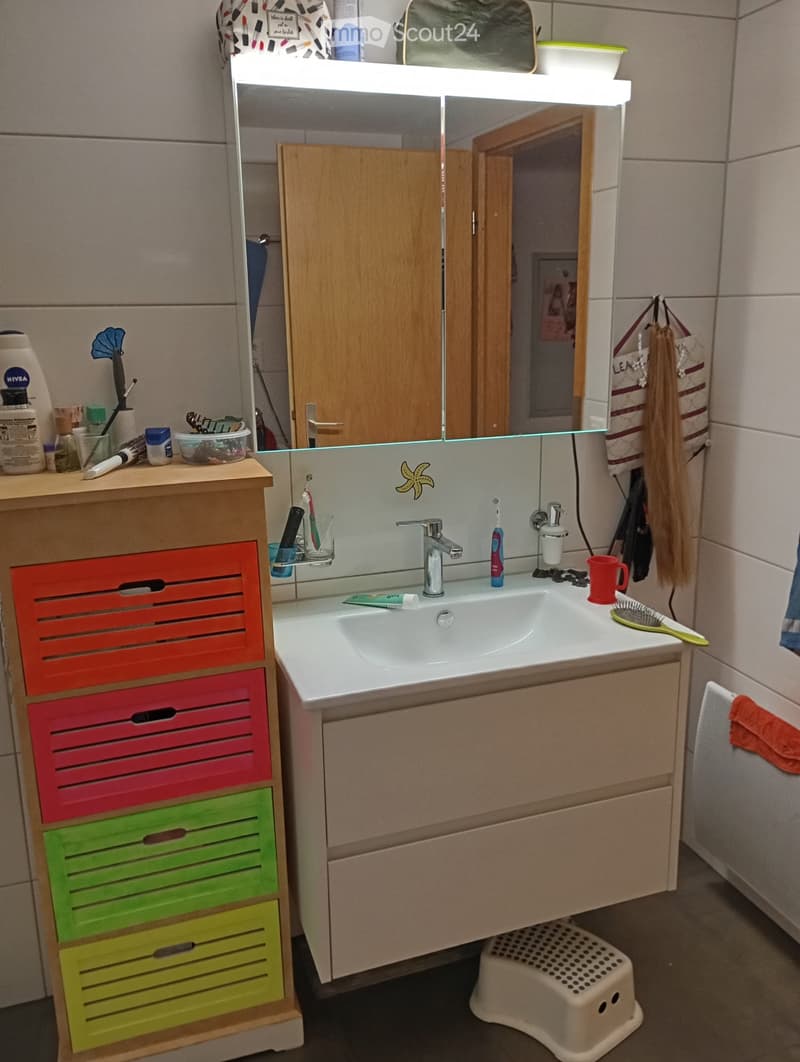 Bathroom with a white sink, mirror, wooden cabinet, colorful drawers, and a radiator.