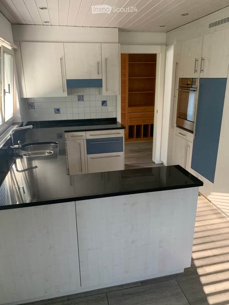 Modern kitchen with white cabinets, black countertops, stainless steel sink, and built-in oven. Features a window and open shelving unit.