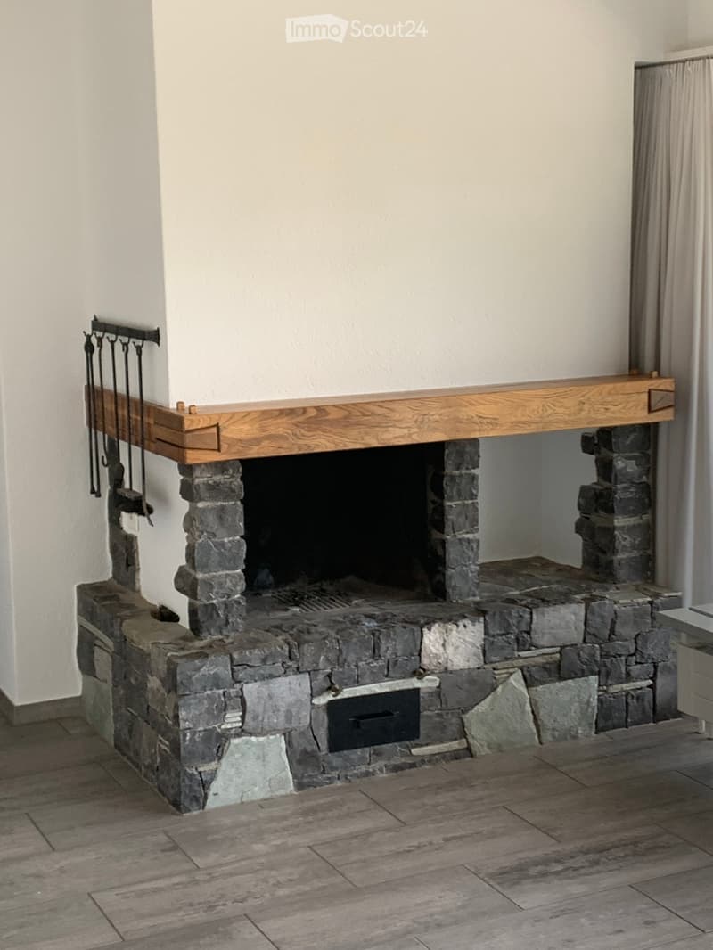 Stone fireplace with wooden mantel and fireplace tools on the left side.