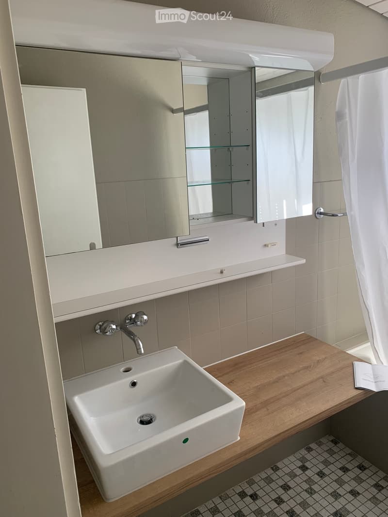 Modern bathroom with a white sink, chrome faucet, mirrored cabinet, wooden countertop, and a white towel hanging on the side.