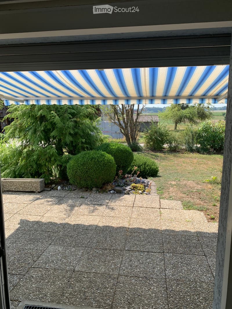 Garden area with gravel, small plants, bushes, and a covered patio with a blue and white striped awning.