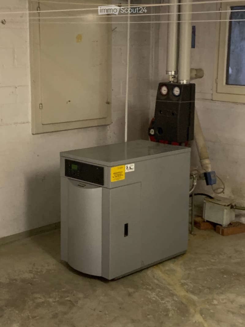 Utility room with a water heater, electrical panel, and various pipes and wiring visible. The floor is concrete, and the walls are unfinished.