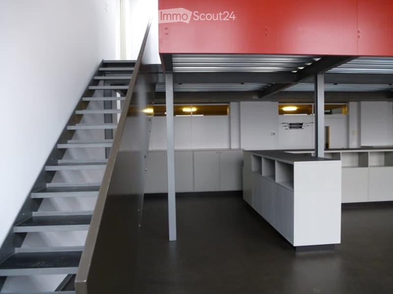 Modern, minimalist interior with a staircase leading upwards, white walls, grey cabinets, and a black floor. No furniture or personal items are present.