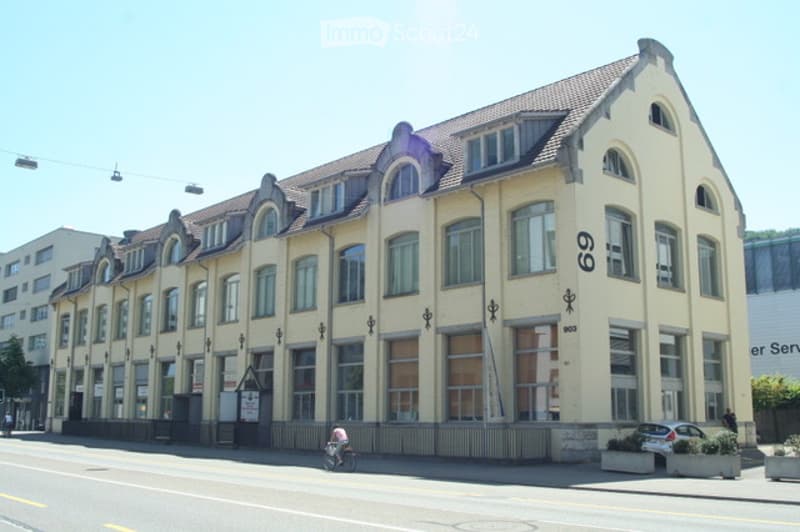 A multi-story building with a cream-colored facade, arched windows, and decorative roofline. The building has a number "69" displayed on the front.