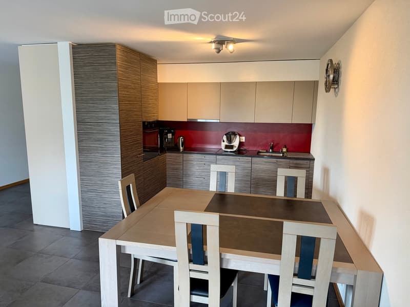 Modern kitchen and dining area with a wooden dining table, four chairs, and various kitchen appliances including a coffee maker, oven, and sink.