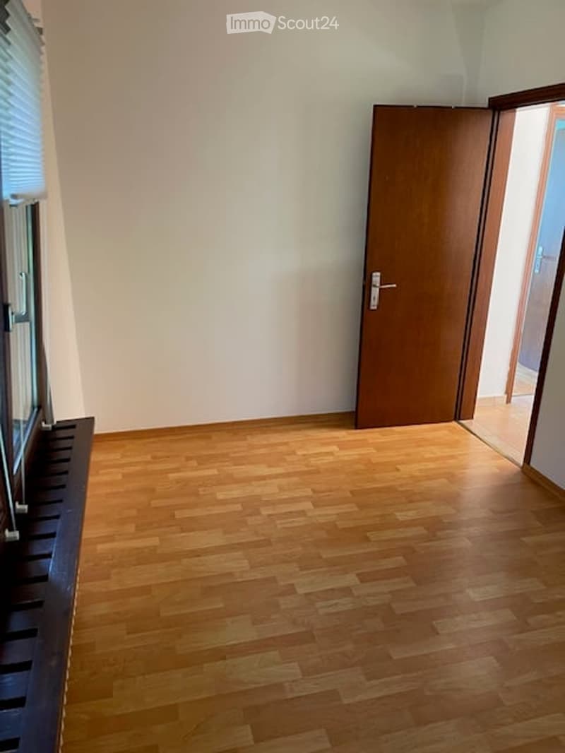 Empty room with wooden flooring, white walls, and a closed wooden door leading to another space.