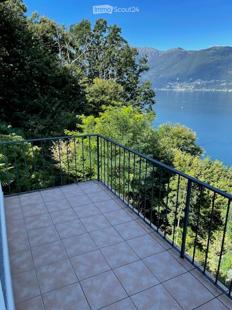 Balcony with tiled floor, metal railing, overlooking a lake and mountains.