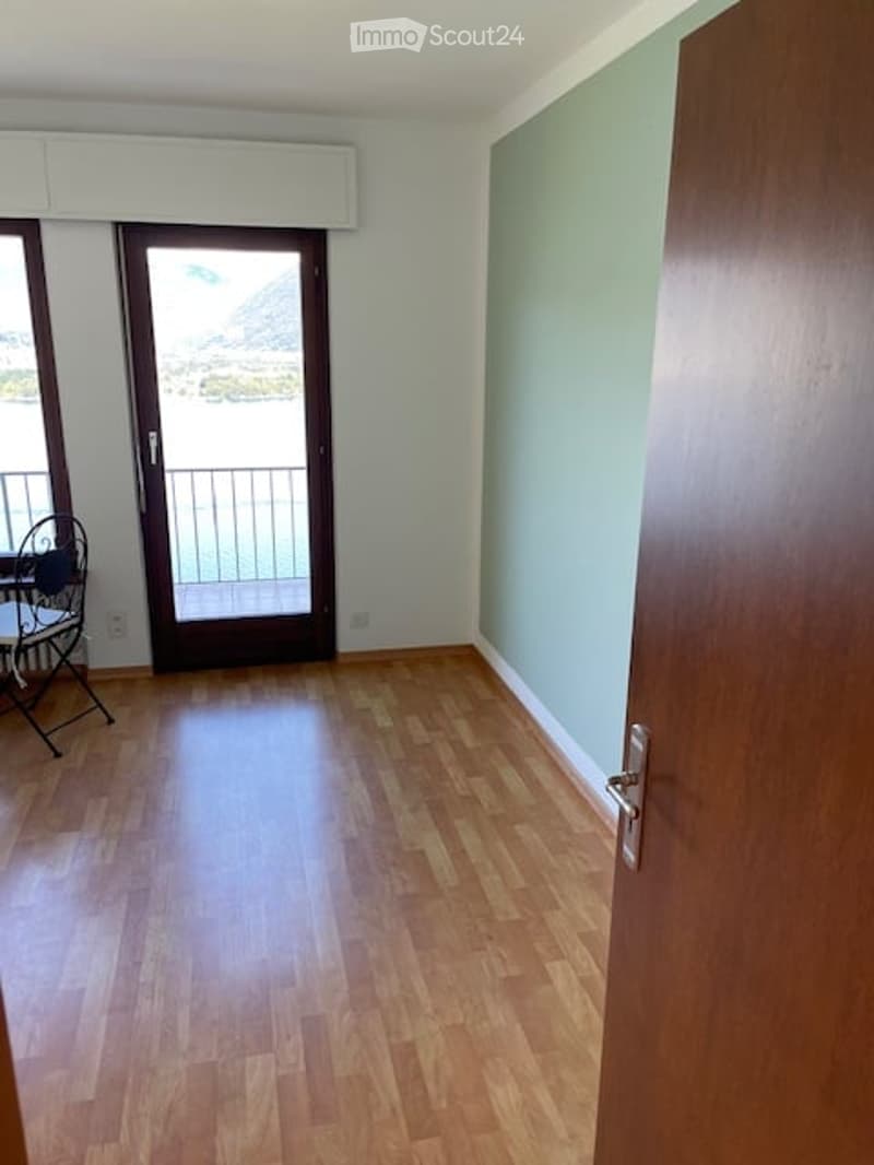 Empty room with wooden flooring, white walls, and a door leading to a balcony with a view.