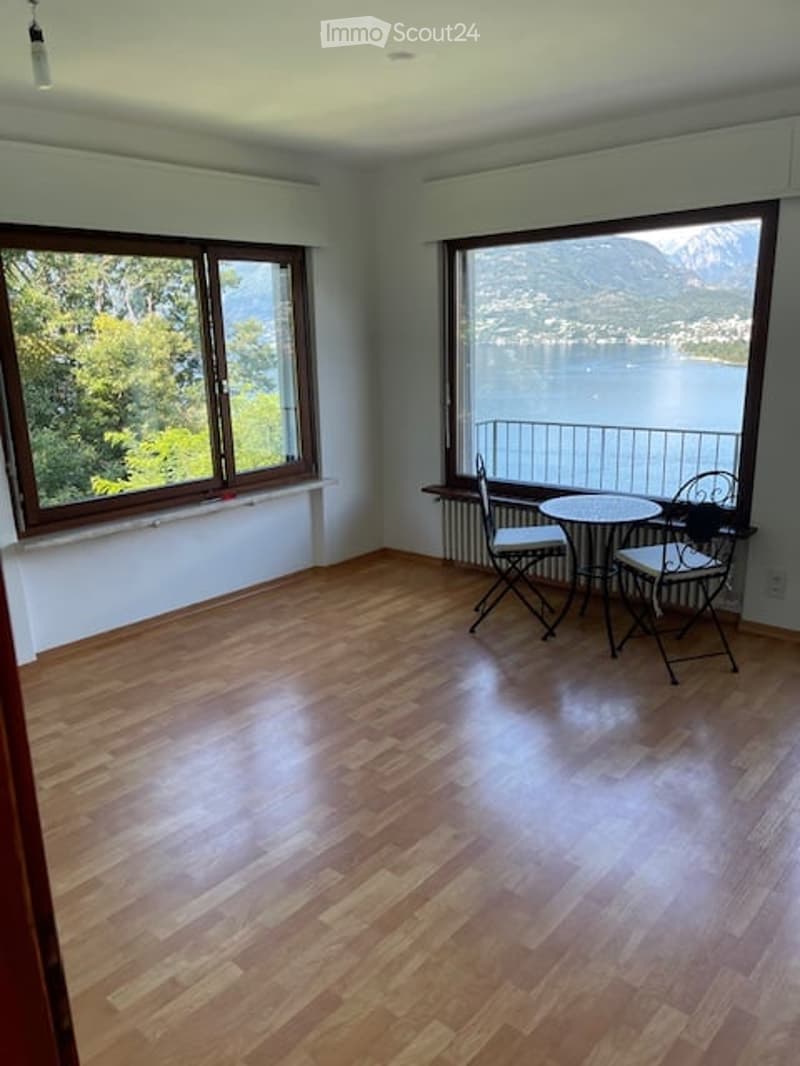 Bright room with wooden flooring, large windows offering scenic views, and a small table with chairs near the window.