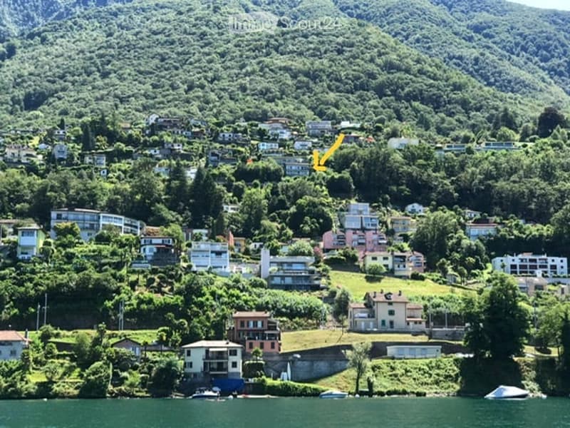 Scenic lakeside town with hillside houses, lush greenery, and a calm lake in the foreground.