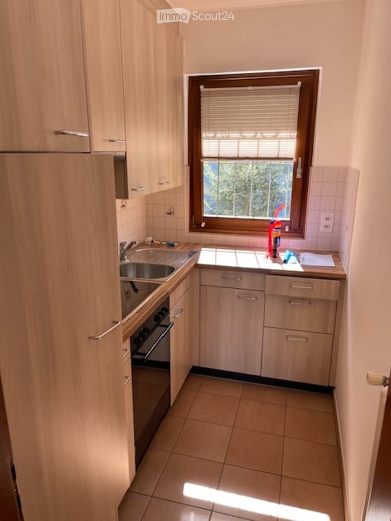 Modern kitchen with light wooden cabinets, stainless steel sink, oven, and a window with blinds.