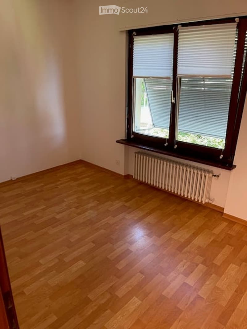 Empty room with wooden flooring, white walls, and a window with blinds. A radiator is placed below the window.