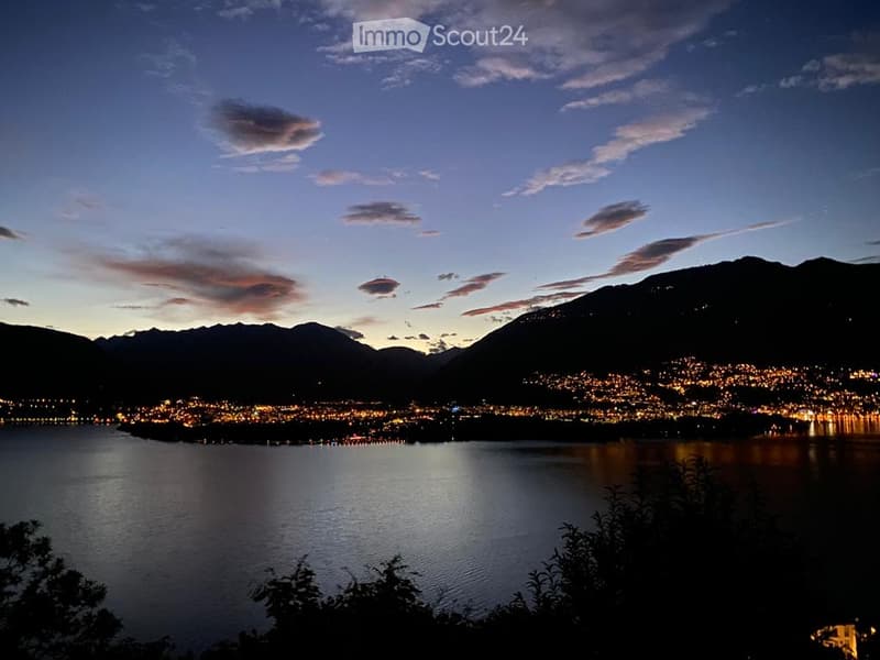 Evening view of a cityscape across a lake, with illuminated buildings and mountains in the background.