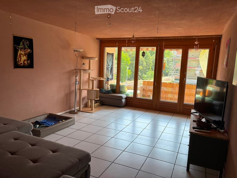 Living room with tiled floor, large windows, cat tree, sofa, television, and a stool.