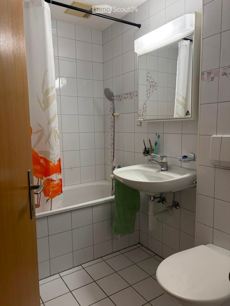 Bathroom with white tiled walls and floor, bathtub, sink, toilet, mirror, and a green towel hanging on the side.