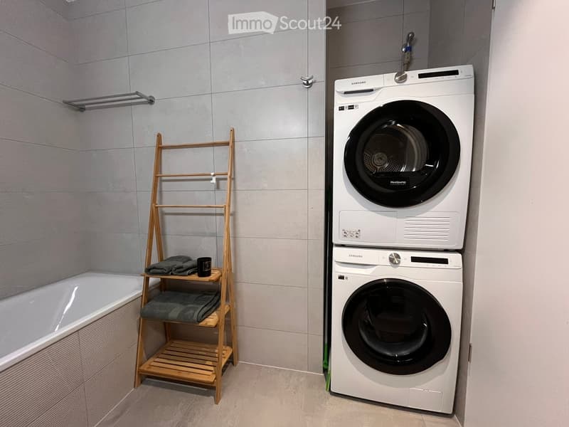 Bathroom with a bathtub, a wooden shelf holding towels, and a stacked washing and drying machine.