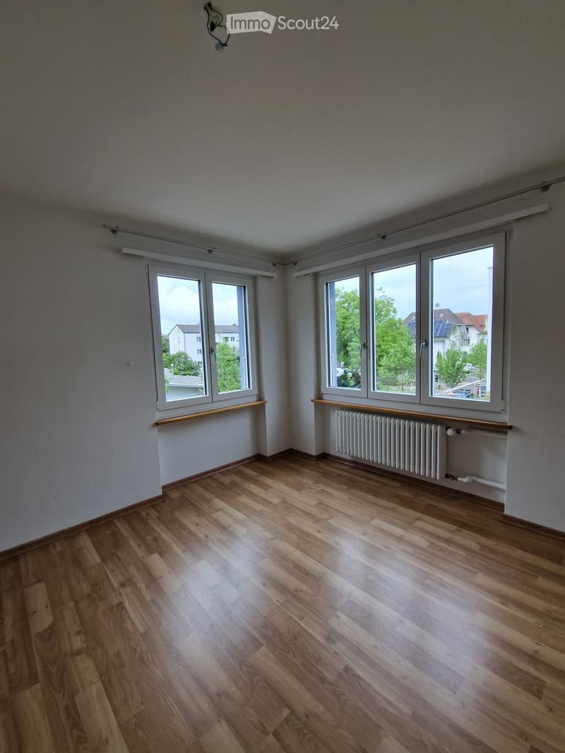Empty room with wooden flooring, large windows, radiator, and wooden window sills.