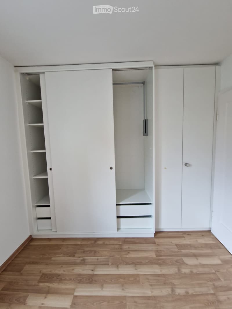 Empty room with light wooden flooring and white built-in wardrobes with shelves and drawers.