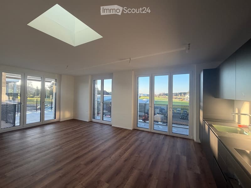 Bright, open room with wooden flooring, large glass doors leading to a patio, and modern ceiling lighting.