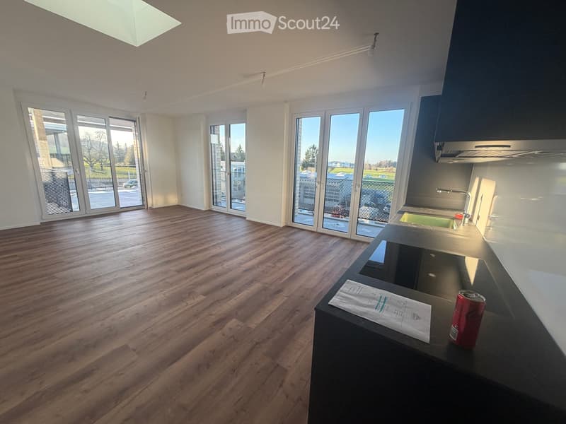 Empty room with wooden flooring, large windows, and a kitchen counter with a sink and faucet.