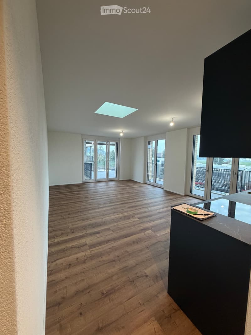 Empty room with wooden flooring, white walls, large windows, and a skylight. No furniture or equipment present.