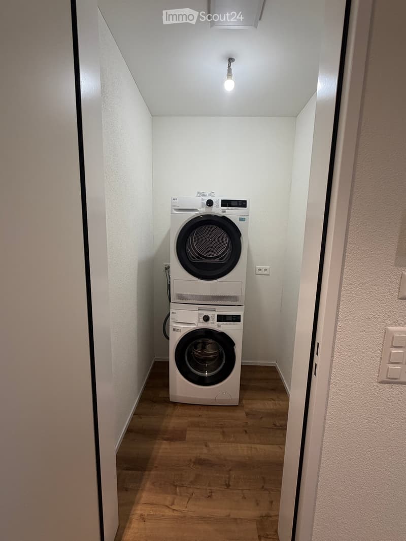 Narrow hallway with wooden flooring, white walls, and a stacked washing machine and dryer unit positioned against the wall.