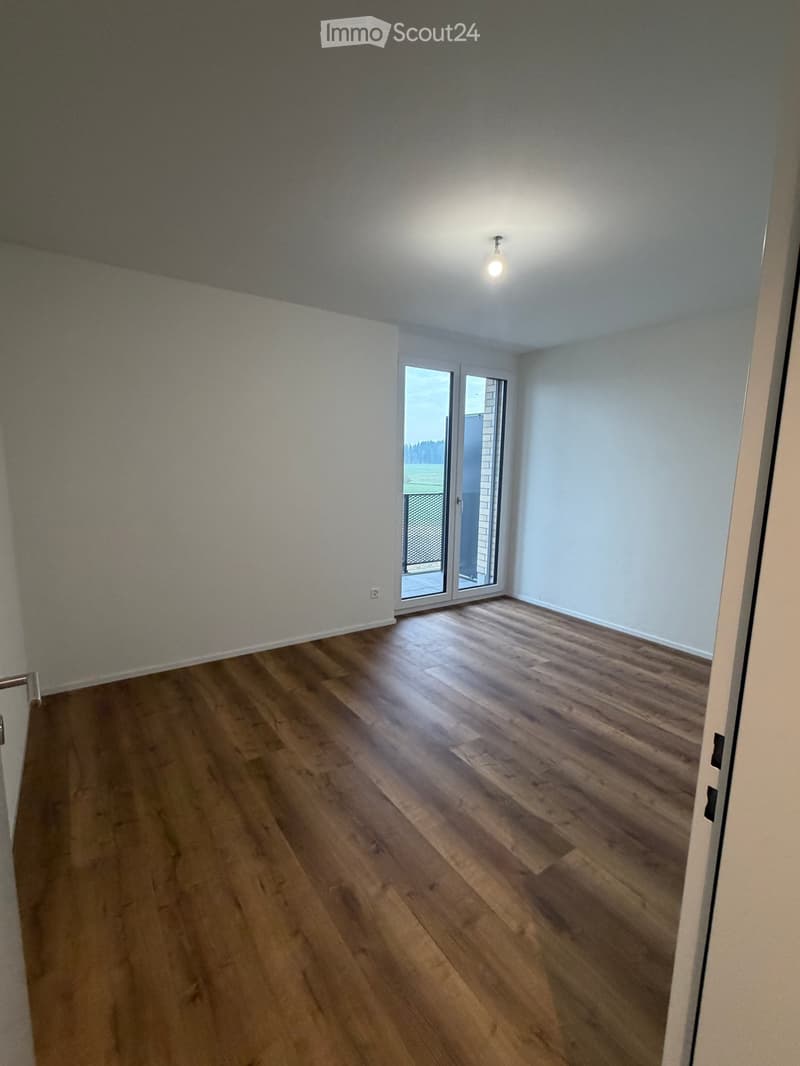 Empty room with wooden flooring, white walls, and a large sliding glass door leading to a balcony.