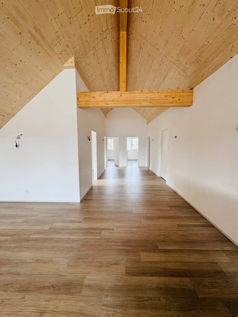 Long hallway with wooden ceiling beams, white walls, hardwood floors, and visible doors and windows.