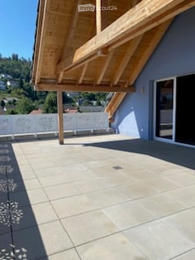Balcony with wooden roof, tiled floor, white railing, and large window opening to the interior.