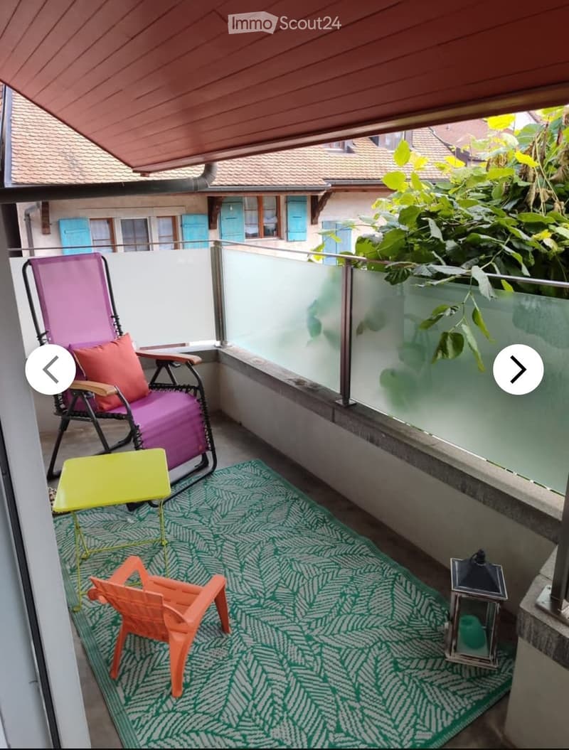 Balcony with a green patterned rug, pink folding chair, small yellow table, orange plastic chair, and lantern.