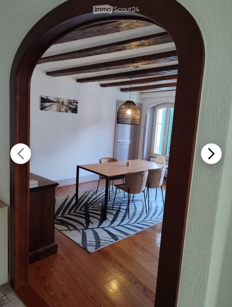 Dining room with wooden floor, dining table, chairs, and a patterned rug.