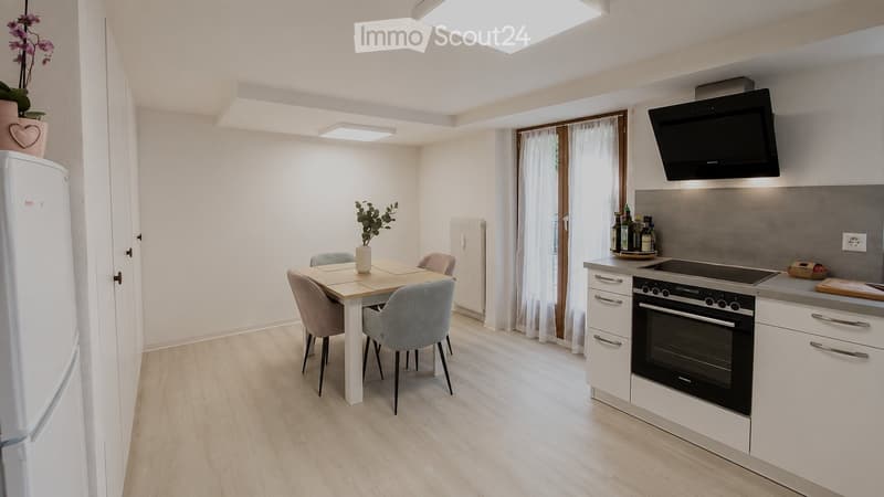 Modern kitchen and dining area with white cabinets, stainless steel appliances, a dining table with four chairs, and a refrigerator. The space features light wood flooring and large windows with white curtains.