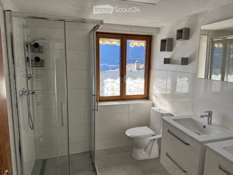 Modern bathroom with a glass-enclosed shower, toilet, sink, and a large window offering a scenic view.