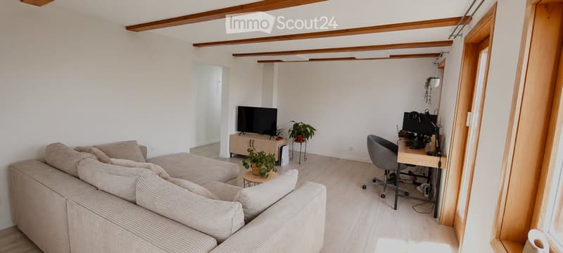 Modern living room with a beige sectional sofa, coffee table, desk with chair, television, and small potted plants.