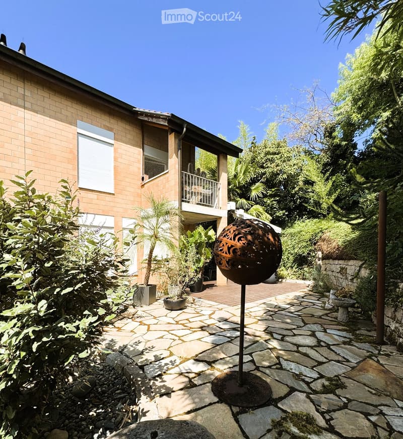 Garden area with stone pathway, decorative metal sphere, potted plants, and a balcony overlooking the space.