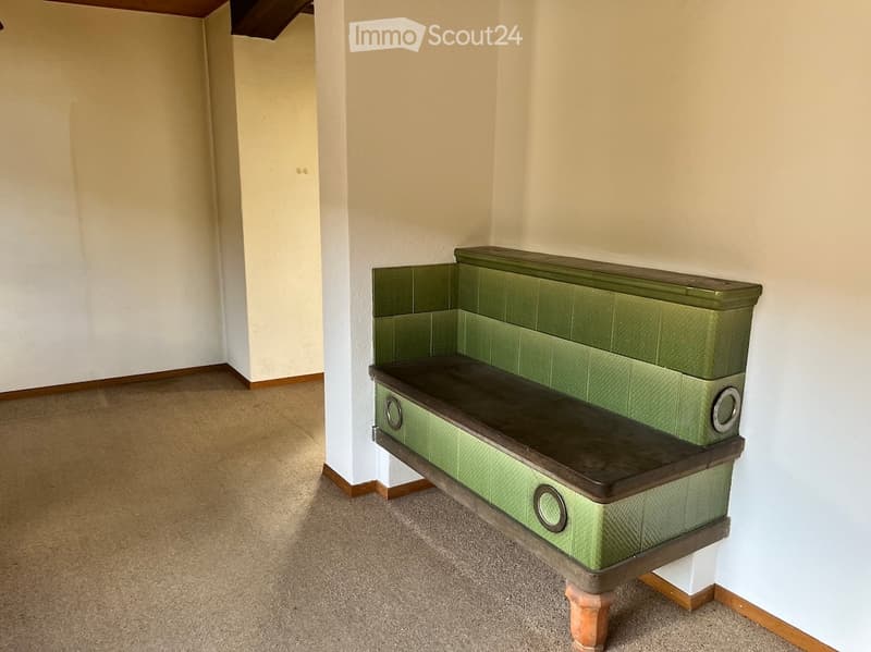 Empty room with beige carpet, white walls, and a green bench with wooden legs and decorative metal accents.