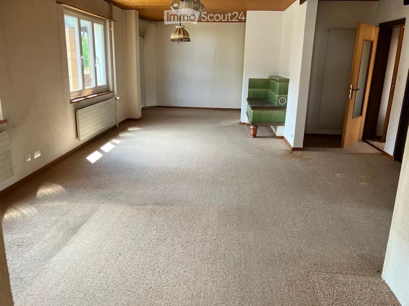 Empty room with carpeted floor, white walls, large windows, and a small green bench in the corner.