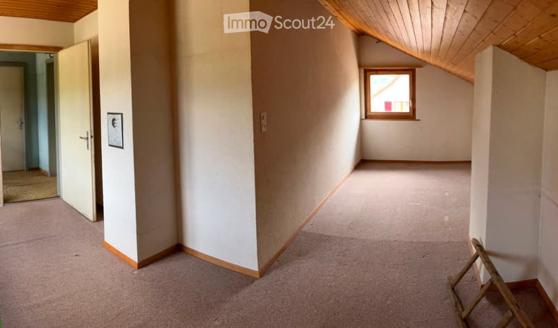 Empty hallway with beige carpeting, white walls, wooden trim, and a small window at the end. A door is open to another room on the left.