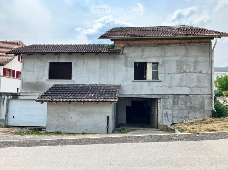 Two-story concrete building with a tiled roof, garage, and weathered facade.