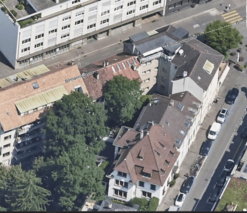 Aerial view of a multi-story residential building complex with red-tiled roofs, surrounded by trees and parked cars on the street.