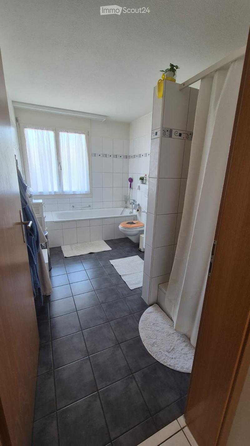 Modern bathroom with dark tiled floor, white tiled walls, bathtub, toilet, shower, and towels.