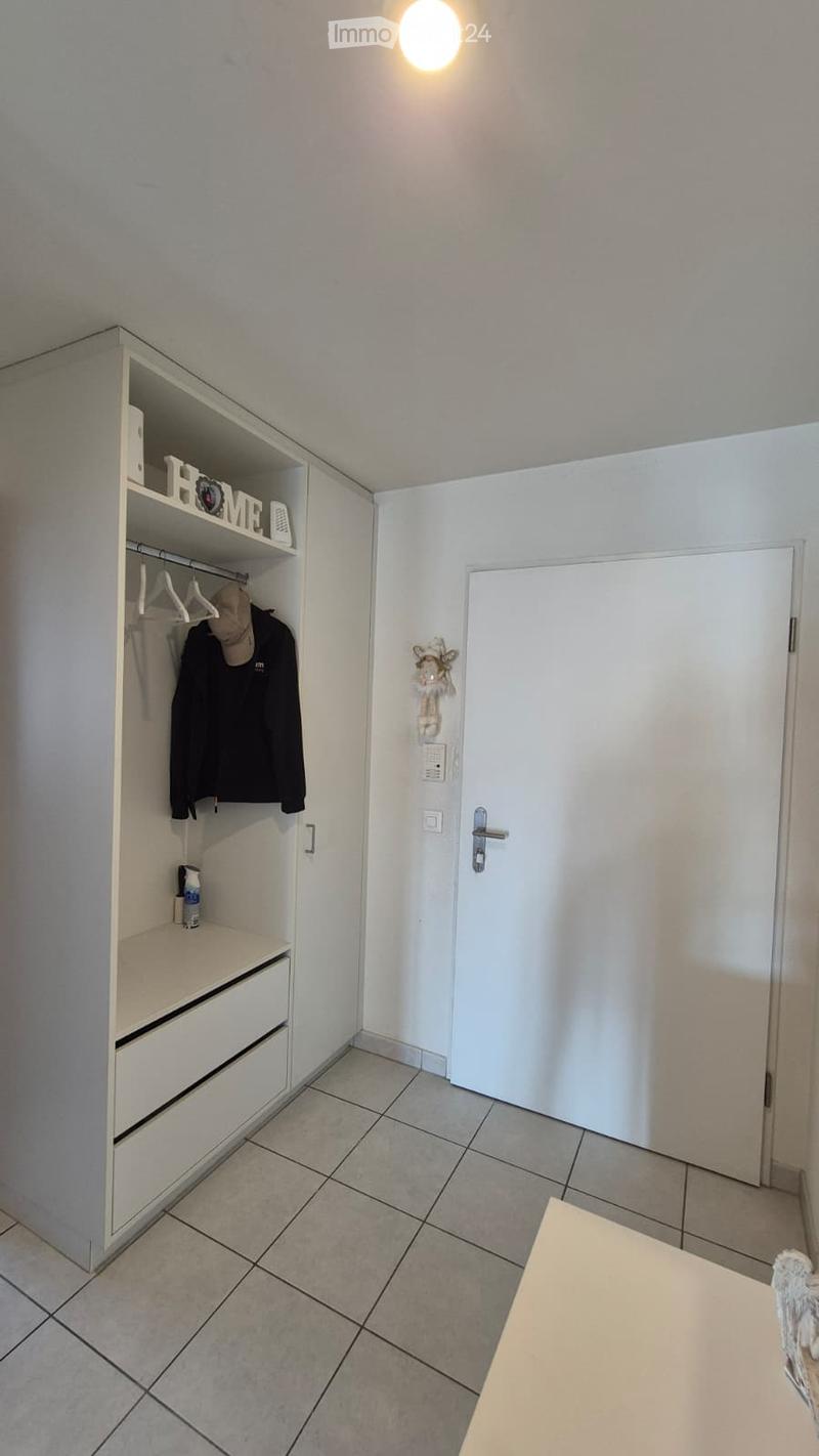 A small, well-lit hallway or entryway with a built-in wardrobe, a shelf with a decorative "HOME" sign, and a coat hanging inside. The floor is tiled, and there is a closed door leading to another room.