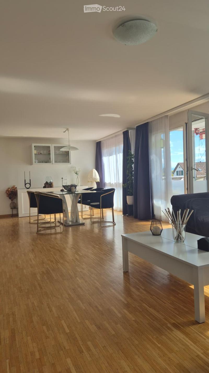 Open-plan living and dining area with wooden flooring, large windows, and modern furniture including a sofa, coffee table, dining table, and chairs.