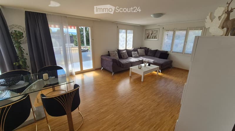 Modern living room with wooden flooring, grey sofa, white coffee table, glass dining table, and chairs.