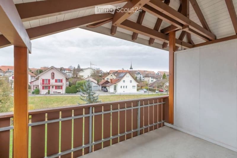 Balcony with wooden beams and railing, overlooking a suburban neighborhood with houses and greenery.