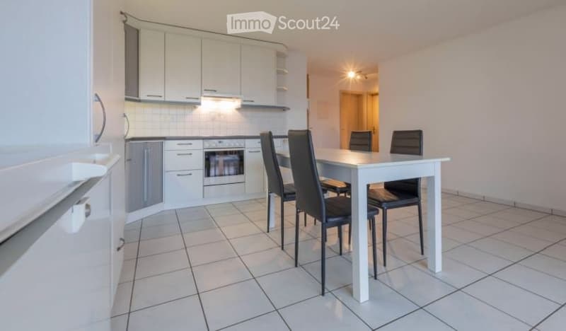 Bright, modern kitchen and dining area with white cabinets, a built-in oven, a refrigerator, and a white dining table with four black chairs.