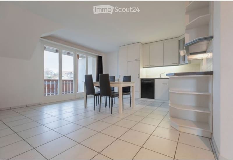 Bright, modern dining area with white tiled flooring, a dining table with four chairs, and a built-in kitchen featuring white cabinets and a dishwasher. Large windows and sliding doors lead to a balcony.