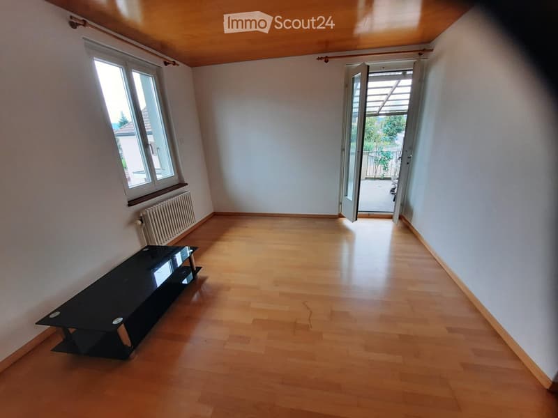 Empty room with wooden flooring, white walls, large windows, and a black table near the window.
