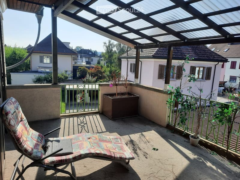 Balcony with a lounge chair, potted plants, and a view of neighboring houses.